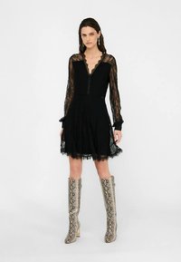 Rochie mini din dantelă neagră, cu mâneci lungi, decolteu în V și fustă evazată. Asortată cu cizme până la genunchi cu imprimeu de șarpe.