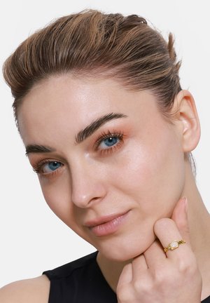 Goldring mit quadratischem Stein, mit einem gedrehten Banddesign. Das Modell hat helle Haut, blaue Augen und nach hinten gekämmtes Haar, trägt ein schwarzes Oberteil.