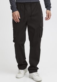 Sorte cargo bukser lavet af bomuld, med elastisk talje, multiple sidelommer og en løs pasform. Parret med hvide sneakers.