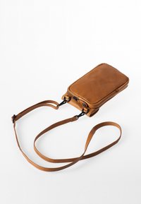 Kompakte braune Leder-Umhängetasche mit Reißverschluss und verstellbarem Riemen, flach auf weißem Hintergrund liegend.