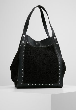 Czarna torba typu tote z teksturowanym materiałowym środkiem, skórzanymi wykończeniami, srebrnymi ćwiekami oraz podwójnymi paskami na ramię, stojąca na białej powierzchni.
