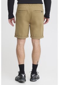 Khaki-shorts med en rullad fåll, elastisk midja och två bakfickor. Svarta sportskor, svarta strumpor och en långärmad topp synliga.