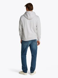 Lichtgrijze hoodie met een trekkoordcapuchon, gecombineerd met blauwe jeans en witte sneakers. De stof lijkt zacht en gestructureerd te zijn.