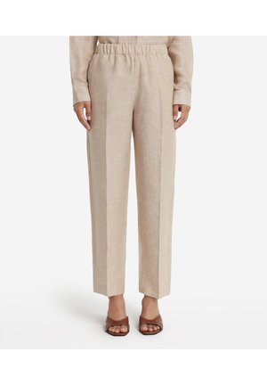 Beigefärgade linnebyxor med rak skärning, elastisk midja och pressveck. Bärs med bruna sandaler med öppen tå.