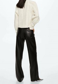 Pull en tricot écru avec détail en maille ajourée, associé à un pantalon large en cuir noir taille haute avec poches et texture lisse.