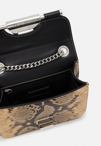 Käärmeenahkakuvioinen laukku, jossa on beigejä ja mustia värejä. Siinä on ketjuhihna, metalliset yksityiskohdat ja musta sisusta vetoketjutaskulla.