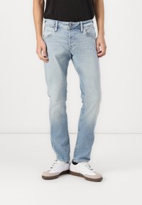 Vaqueros de denim azul claro con un corte recto, cinco bolsillos y costuras en contraste. Llevados con zapatillas blancas con acentos grises.