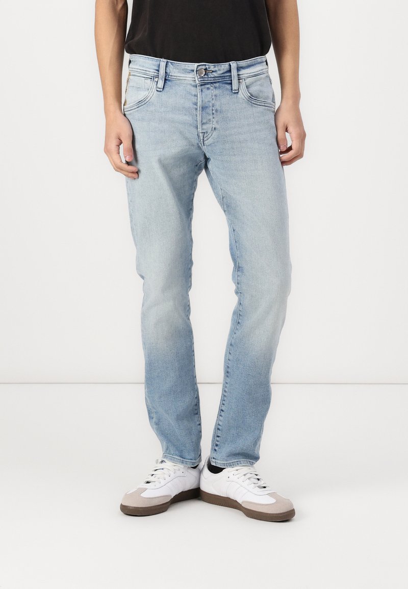 Vaqueros de denim azul claro con un corte recto, cinco bolsillos y costuras en contraste. Llevados con zapatillas blancas con acentos grises.