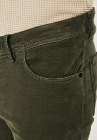 Kaki Cordhosen aus strukturiertem Stoff mit einer Vordertasche, abgesteppten Nähten und einem Knopfakzent neben dem Bund.