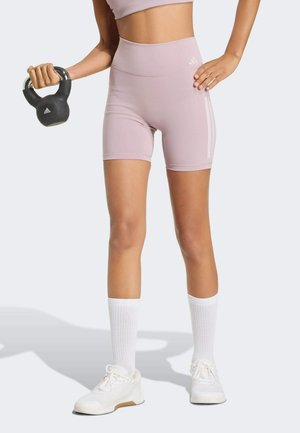Helle pinkfarbene, hoch taillierte Sportshorts mit tonalen Seitenstreifen, kombiniert mit weißen knielangen Socken und weißen Sneakers. Hantelgriff in der Hand gehalten.