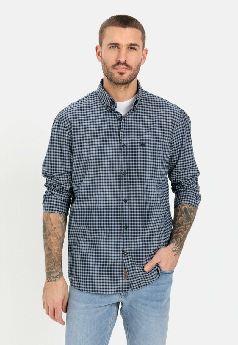 Blauw en wit geblokt overhemd met kraag, enkel borstzakje, opgerolde mouwen en een logo detail op de borst. Draagt met lichte jeans.