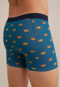 Kék boxeralsó, puha szövetből készült, sárga és piros hot dog mintázattal. Sötétkék, rugalmas derékrésszel.