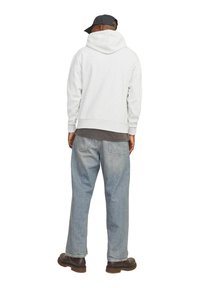 Sudadera de algodón gris claro con bolsillo canguro y capucha ajustable con cordón, combinada con jeans de mezclilla azul de corte holgado y calzado marrón.