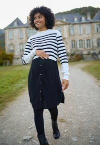Sort knap-op kjole med høj slids, kombineret med en cropped hvid og sortstribet sweater. Model iført sorte leggings og ankelstøvler.