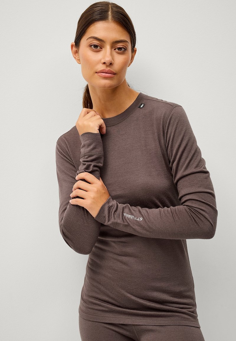 Langsleeve bruine top van zachte stof, met een ronde halslijn en een logodetail op de linkermouw. Glad textuur en getailleerd ontwerp.