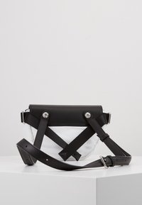 Borsa in pelle nera e tessuto bianco con cinturini incrociati, hardware argentato e tracolla regolabile. Presenta una forma strutturata e un finish opaco.