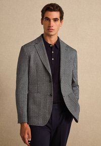Blazer met houndstooth-patroon in grijs en marineblauw, met een sluiting met twee knopen, notch-lapels en een zak, gecombineerd met een donkere polo.