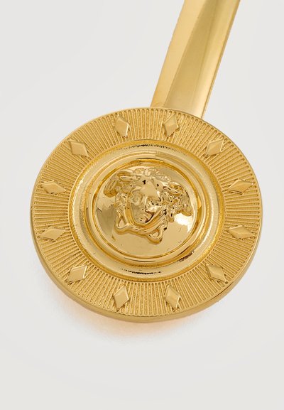 Barrette ronde en or avec une tête de Méduse en relief au centre, entourée de petits accents en forme de losange sur un fond texturé.