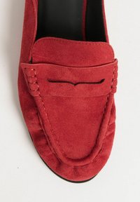 Røde ruskinds loafers med en syet design, en rund tå og et dekorativt bånd over vristen. Glat sort sål.