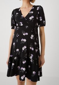 Svart omlottklänning med blommönster i lila och vitt, korta puffärmar, midjeband och volangkant. Slät tygtextur.