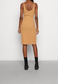 Ribbad, figurnära stickad klänning i kamelfärg, med V-rygg och tunna remmar, kombinerad med svarta ankellånga stövlar med tjocka klackar.