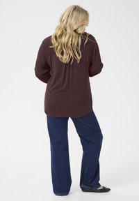Long-sleeve maroon top with a relaxed fit, paired with dark blue wide-leg jeans and black flat shoes, viewed from the back.