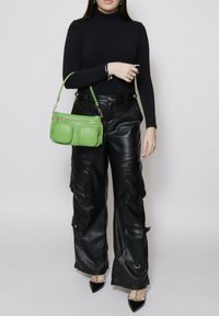 Groene leren handtas met twee voorzakken, gouden hardware en een korte schouderriem, gecombineerd met zwarte leren cargo-broeken en zwarte hakken.