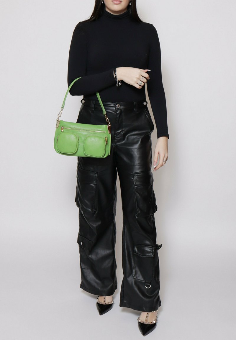 Groene leren handtas met twee voorzakken, gouden hardware en een korte schouderriem, gecombineerd met zwarte leren cargo-broeken en zwarte hakken.