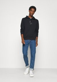 Sudadera negra con cordones, combinada con jeans de mezclilla azul claro y zapatillas blancas. Diseño sencillo, material de algodón, mangas largas.