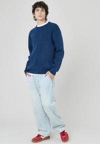 Pull en maille bleu marine à col rond, associé à un jean baggy bleu clair et des baskets rouges. Texture douce, coupe décontractée.