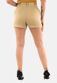 Shorts en kaki taille haute avec ourlets roulés, tissu texturé et ceinture tressée. Des escarpins noirs avec des accents en nœud complètent la tenue.