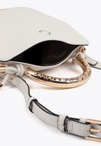 Ljusgrå handväska med ett metalliskt guldhandtag, olåst för att avslöja ett svart inre och en justerbar rem.