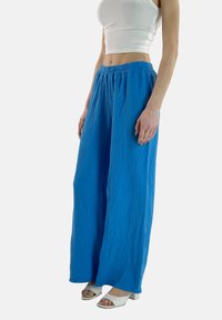 Pantaloni a gamba larga blu realizzati in tessuto texturizzato, con vita elastica. Abbinati a sandali bianchi con tacco.