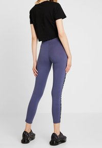 Skrojona czarna koszulka i fioletowe legginsy z bocznymi akcentami logo. Legginsy charakteryzują się gładką teksturą i dopasowanym krojem. Czarne sneakersy.