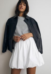 Jachetă din piele neagră, hanorac gri și fustă din balon albă. Textură netedă, design stratificat, cu talie ajustată și tiv voluminos.