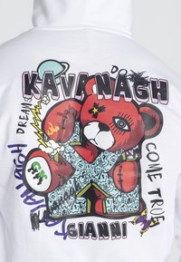 Sudadera blanca con un gráfico colorido de un oso de dibujos animados, con texto en negrita y varios diseños que incluyen estrellas, rayos y una mariposa.