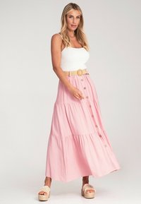 Rosa gestufte Maxikleid mit Knöpfen, aus Baumwollmaterial und einem geflochtenen Gürtel. Das Model trägt Plattform-Sandalen; das Kleid reicht bis zum Knöchel.