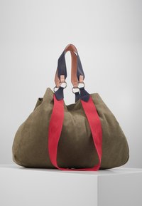 Große olivgrüne Stofftasche mit roten Trägern und marineblauen Lederdetails. Verfügt über silberne Beschläge und eine weiche, abgerundete Form.