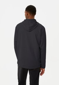Giacca nera con cappuccio, realizzata in tessuto liscio e opaco; presenta tasche laterali e una vestibilità rilassata, che si estende fino a metà fianchi. Cappuccio con texture per un tocco di dettaglio in più.