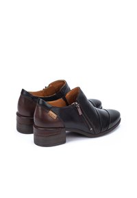 Bottines en cuir noir avec un talon marron, dotées d'une fermeture éclair à l'avant, de coutures arrondies et d'un design de bout arrondi.