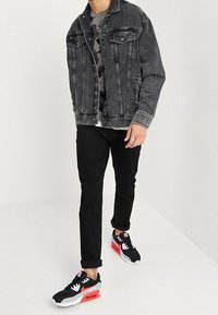 Black denim jacket, gray camouflage sweater, black pants, and black sneakers with red accents. Outfit emphasizes casual, layered styling.