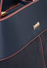 Borsa a mano blu scuro con una parte superiore in pelle liscia con dettagli arancioni, corpo in suede testurizzato e logo del marchio dorato.