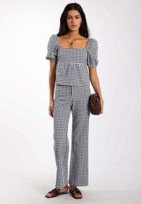 Haut court en vichy noir et blanc avec des manches bouffantes, associé à un pantalon large assorti. Sac à main texturé marron et sandales à lanières en complément.