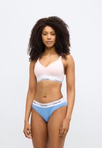 Ροζ ελαφριά μπραλέτα με V-λαιμόκοψη, με λευκή ταινία με το λογότυπο "Calvin Klein". Μπλε σλιπ hipster με λευκή ελαστική μέση.