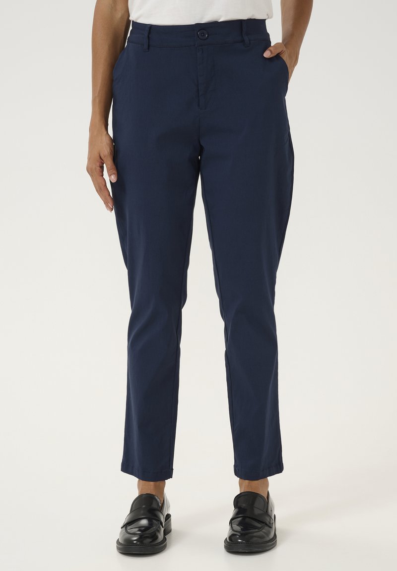 Pantalons légers bleu marine avec une coupe slim, dotés d'une fermeture à bouton, de poches latérales et d'une texture lisse. Accentués par des chaussures noires à enfiler.