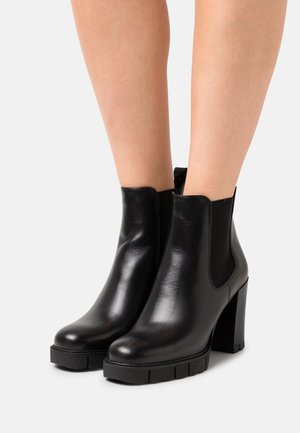 Bottines en cuir noir avec talons hauts à bloc, panneaux latéraux élastiques et semelles texturées. Finition lisse avec des orteils ronds et des coutures minimales.