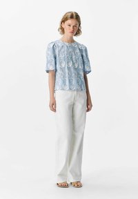 Blusa bordada de color azul claro con mangas cortas abullonadas, que presenta un patrón floral, combinada con pantalones de pierna ancha blancos y sandalias sencillas.