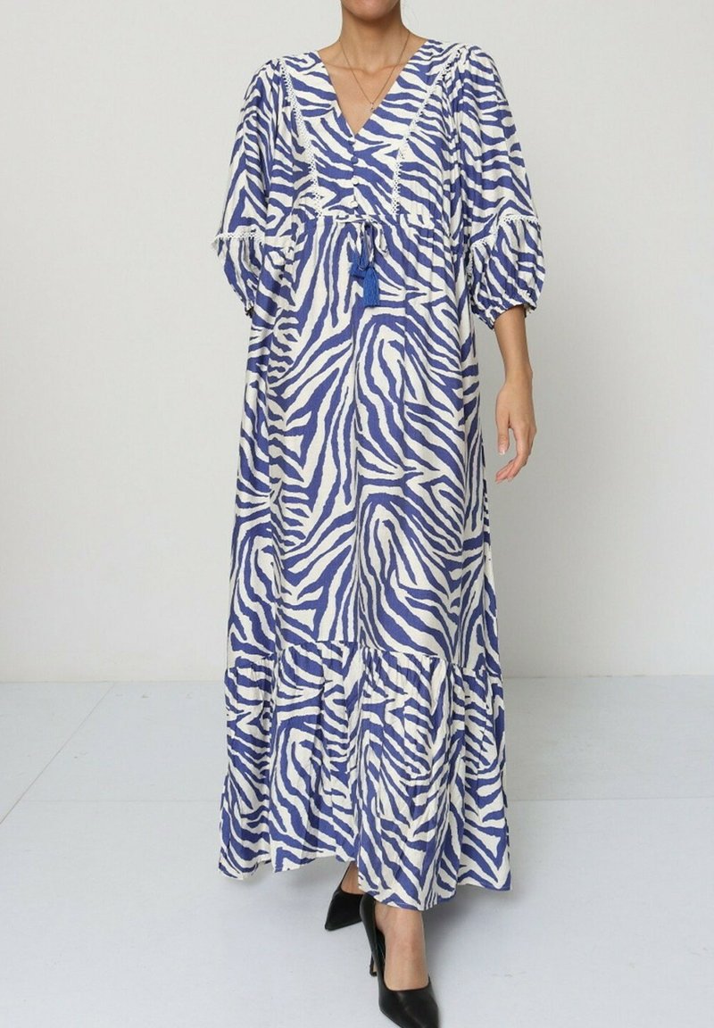Robe maxi à motifs zèbre bleu et blanc avec décolleté en V, manches bouffantes, taille cintrée et jupe à volants. Le tissu semble texturé et léger.