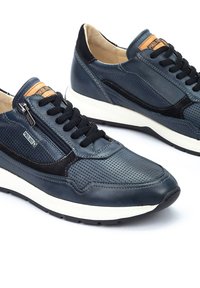 Modré kožené tenisky s perforovaným designem a černými akcenty, vybavené bočním zipem, černými tkaničkami a bílou gumovou podrážkou.