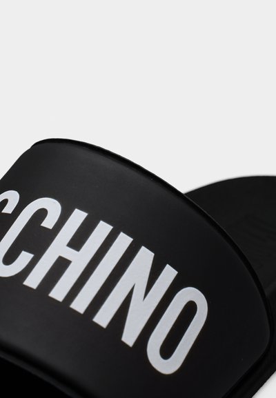 Μαύρο σανδάλι με φαρδιά λουρί που φέρει το έντονο λευκό μερικό λογότυπο "MOSCHINO".